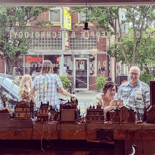 A view through the original storefront window toward neighbors on Main Street, with miniature buildings on the inside sill.